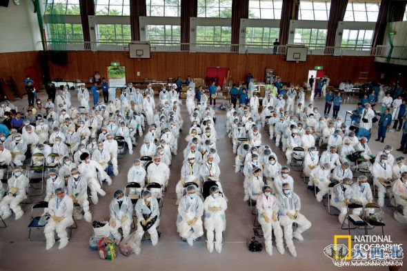 6月8日，廣野町的一個(gè)體育館里，身穿防護(hù)服的居民正聽人們向他們介紹注意事項(xiàng)，之后他們將在專人護(hù)送之下回到家中，取回幾樣小物品。（巴士上沒有擱置大件物品的空間。）一名當(dāng)?shù)毓賳T稱，盡管來的路上戒備森嚴(yán)，但在排除污染的過程中（處理鞋套、防護(hù)服、帽子和口罩，并對人們進(jìn)行放射物排查），所有人和物品都被放了一馬。